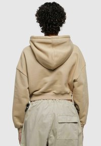 Beskjært beige hettegenser med romslig hette, tilpassede mansjetter og en myk tekstur, kombinert med lyse cargo-bukser med sidelommer.