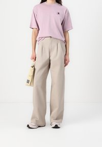 Light purple short-sleeve shirt with a small logo, paired with beige wide-leg pants. A beige tote bag and sneakers complete the look.
