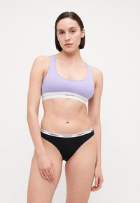 Svetlofialový rebrovaný bralet s bielym pásom; čierne bikini s bielym pásom s logom Calvin Klein. Jednoduchý, priliehajúci dizajn.