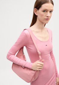 Ružičasta torba preko ramena s glatkom teksturom, suptilnim sjajem, podesivim remenom i zippered džepom s brendiranim akcentom.