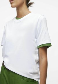Hvid bomulds t-shirt med en rund grøn kant, parret med grønne teksturerede bukser. Korte ærmer og afslappet pasform.