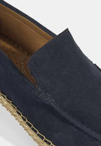 Marine blauwe suède instapschoen met een afgerond ontwerp, voorzien van een espadrille jutezool en een beige leren voering met perforaties.