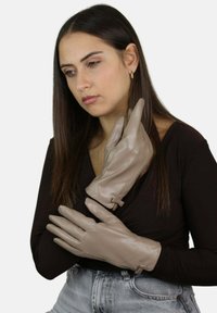 Beżowe rękawiczki ze skóry o gładkim wykończeniu, eleganckim designie i ozdobnych przeszyciach. Wyposażone w cienki pasek do regulacji na nadgarstku.