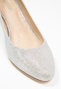Chaussure plate pailletée argentée avec bout pointu et doublure intérieure beige sur fond blanc.
