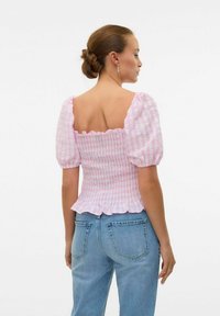 Smokket rosa og hvitstripete topp med korte pufferm, firkantet bak og parret med lyseblå denimjeans. Strukturert stoff.