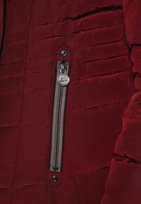 Vinröd vadderad jacka med en silverfärgad dragkedjeficka och mörkgrå dragkedja, med horisontella sömmar och en slät tygstruktur.