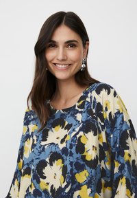 Top de estampado floral en azul, amarillo y negro. Presenta un escote redondo y un corte holgado con mangas amplias. Textura de tela suave.