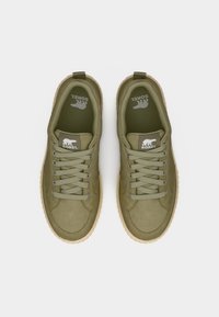 Ζευγάρι ελιά πράσινα αθλητικά παπούτσια Sorel με μπεζ σόλες, άνω όψη, με κορδόνια και λογότυπο πολικής αρκούδας στη γλώσσα και στις εσωτερικές σόλες.