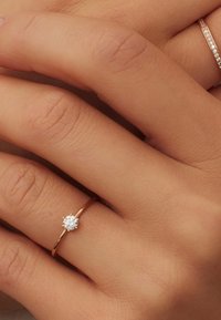 Gouden ring met een enkele ronde diamant, met een gladde band en gepolijste oppervlakte, geplaatst op een hand met subtiele huidtextuur.