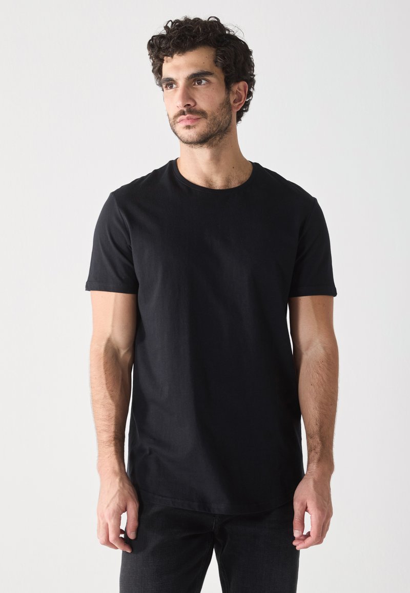T-shirt noir à manches courtes en tissu lisse avec un col rond, associé à un jean foncé. Présente un design minimaliste et une coupe régulière.