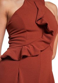 Vestido color óxido con un solo tirante, que presenta detalles de volantes a lo largo del cuerpo. Tejido suave con una silueta ajustada y pliegues.