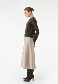 Mørkegrå strikket sweater, beige satin midi-nederdel og sorte højhælede støvler. Model poserede i profil mod en ensfarvet hvid baggrund.