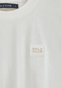 Witte katoenen sweatshirt met een ribgebreide hals. Heeft een vierkante logo patch met "POLO CLUB" in beige tekst. Zachte textuur, casual ontwerp.