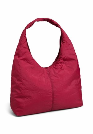 Borsa a spalla morbida, grande, di un rosso intenso con manico largo e cucitura visibile al centro, in piedi contro uno sfondo semplice.