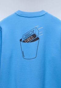 Μπλε φούτερ με εικόνα κάδου απορριμμάτων που περιέχει ένα ψηφιακό ξυπνητήρι, εμφανίζοντας τις λέξεις «SNOOZE» και «TIRED». Μαλακή υφή.