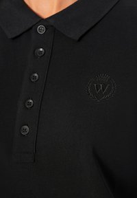 Polo shirt nera in tessuto strutturato, con patta dei bottoni, bottoni neri e un sottile logo ricamato sul petto.