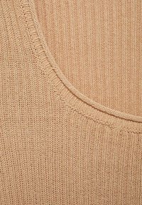 Acercamiento de una tela de punto beige con textura acanalada y detalles en el borde del cuello redondeado.