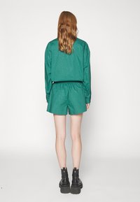 Camisa verde de manga corta y pantalones cortos a juego con una cinturilla elástica, con detalles brillantes. Combinado con botas gruesas negras.