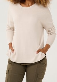 Hellbeiger gerippter Pullover mit rundem Halsausschnitt und Seitentaschen, kombiniert mit olivgrünen Cargohosen mit Seitentaschen.