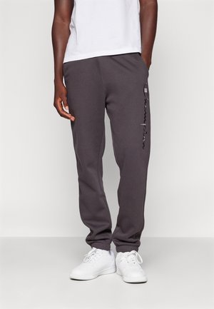 Szare spodnie dresowe z elastycznymi ściągaczami, kieszeniami po bokach oraz detalem z logo na lewej nogawce. Połączone z białymi sneakersami i prostą białą koszulką.