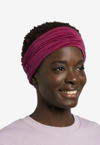 Diadema de tela morada con una textura suave, que presenta pliegues superpuestos. La persona que la lleva tiene el cabello corto y rizado y viste una sudadera de color morado claro.