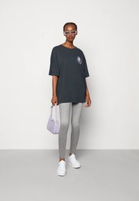 Overdimensjonert mørkegrå t-skjorte med en solgrafikk, kombinert med lysegrå leggings, hvite joggesko og en liten lavendelfarget veske.