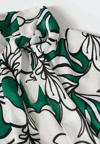 Blouse verte et blanche avec imprimé floral abstrait noir, dotée d'un détail de col noué sur tissu lisse.
