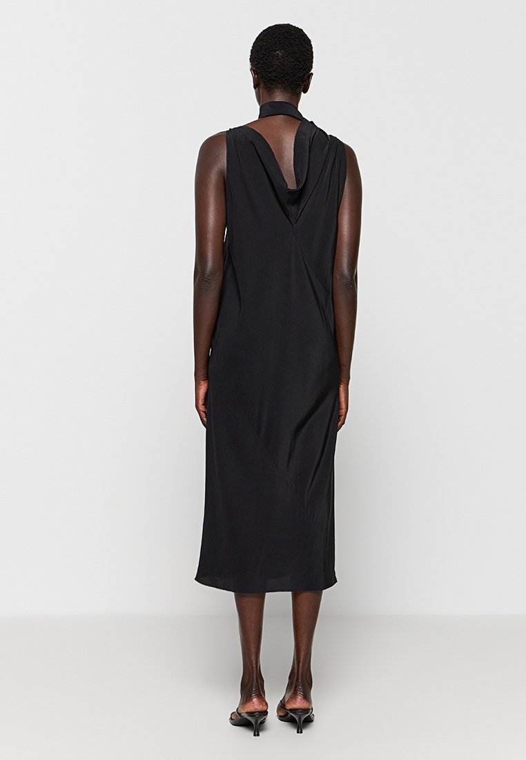 Czarna sukienka bez rękawów z drapowanym tyłem, o długości do kolan, gładkiej fakturze i dekolcie halter. Prosta i elegancka sylwetka.