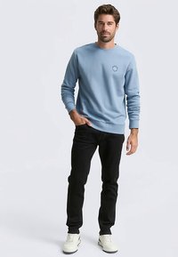 Světlounká modrá mikina z měkké látky s kulatým výstřihem, žebrovanými manžetami a lemem. Kombinována s černými džíny a bílými teniskami.