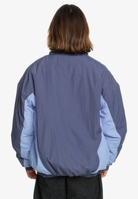 Oversized jacket featuring a dark navy body and light blue panels, made of smooth, lightweight fabric with elastic cuffs and hem.