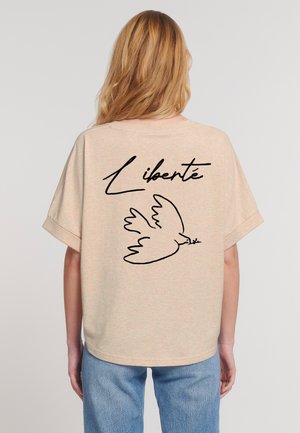 Beige oversized t-shirt with short sleeves featuring a black outline drawing of a dove and the word "Liberté" on the back.