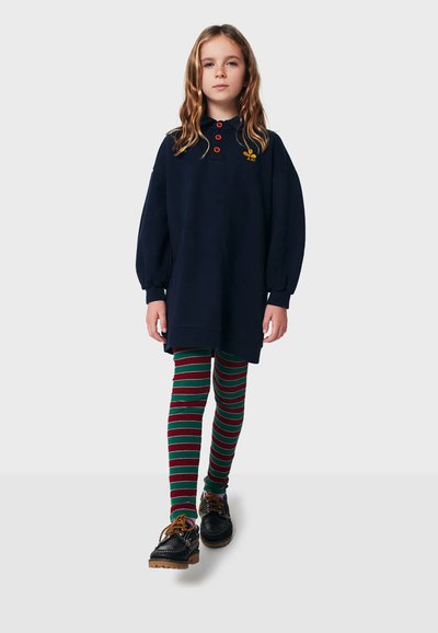 Robe polo oversize marine avec boutons rouges, associée à des leggings rayés rouges et verts et à des chaussures noires avec une semelle épaisse.