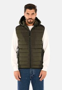 Gilet imbottito verde con zip frontale, cappuccio e due tasche laterali con zip; tessuto testurizzato con cuciture orizzontali e dettagli neri sulle spalle.