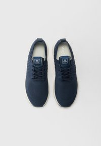 Baskets de sport bleu marine avec un dessus en maille texturée, dotées d'une languette, de lacets et d'une semelle blanche. Étiquette de logo sur la languette.