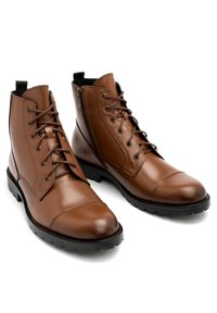 Brązowe skórzane botki za kostkę z okrągłym noskiem, sznurowanym przodem i zamkiem błyskawicznym z boku. Posiadają czarne gumowe podeszwy i złote metalowe oczka.