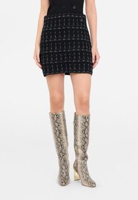 Gonna mini nera in tweed con un motivo a quadri texturizzato abbinata a stivali fino al ginocchio con stampa camoscio metallica a serpente e tacco a blocco.