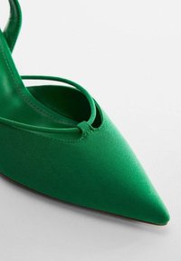 Chaussure en satin vert à bout pointu avec un design bride arrière, présentant un détail découpé et une texture lisse. Semelle robuste et plate.