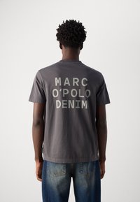 Grijze katoenen t-shirt met grote witte tekst "MARC O'POLO DENIM" op de achterkant. Ronde hals met korte mouwen, gecombineerd met denim jeans.