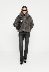 Grå faux fur jakke med højt krave og knaplukning, parret med mørke jeans og spidse sorte sko. Accessories inkluderer en sort taske.