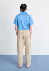 Light blue short-sleeved polo shirt, beige loose-fitting pants with elastic waist, and white sneakers with red accents, viewed from the back.