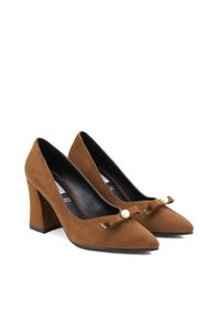 Scarpe con tacco alto in suede marrone, con punta affusolata, caratterizzate da un dettaglio a fiocco con perla e un tacco a blocco largo.