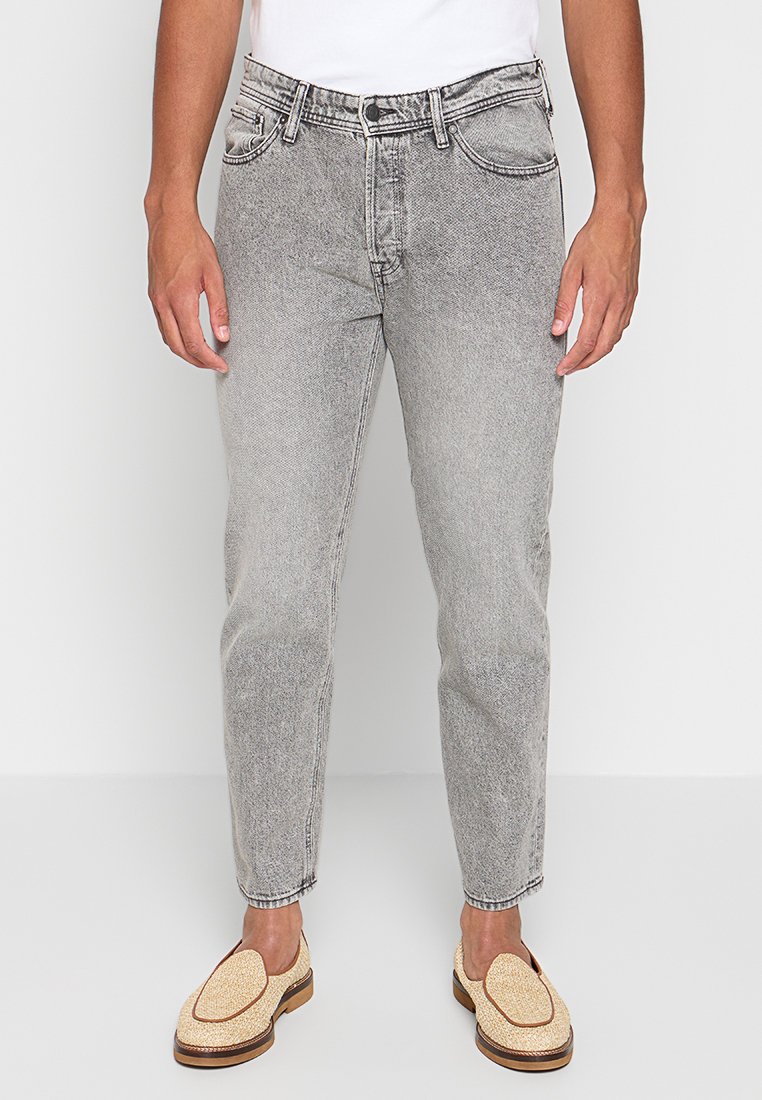 Hellgraue Jeans aus Denim mit geradem Schnitt, fünf Taschen, sichtbarem Nähten und einer leicht abgedunkelten Textur, kombiniert mit beigen Slippern.