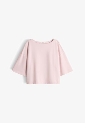 Haut rose pâle, coupe ample, manches courtes larges et encolure ronde, présenté à plat sur un fond blanc.