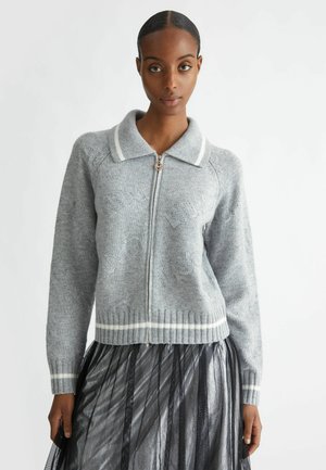 Maglione grigio a maglia con zip frontale, colletto bianco e orlo a coste. Presenta una superficie strutturata e un sottile logo decorativo in tutta la sua lunghezza.