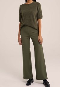 Olivgrön, kortärmad stickad tröja i kombination med olivgröna vida byxor. Byxorna har en slät textur, och outfiten kompletteras med svarta loafers.