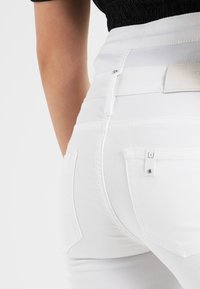 Jeans blancos de denim, con un ajuste ajustado, cierre de cremallera y dos bolsillos traseros con una pequeña etiqueta de logo en uno de los bolsillos.