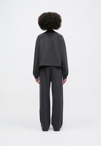 Σκούρο γκρι φαρδύ φούτερ με ράγλες μανίκια, συνδυασμένο με αντίστοιχα χαλαρά παντελόνια που διαθέτουν πίσω τσέπη. Απαλή υφή.