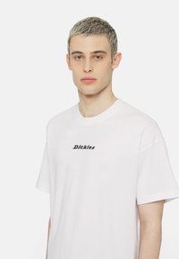 White cotton t-shirt with a crew neck and short sleeves. Features a black "Dickies" logo positioned centrally on the chest.