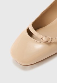 Beige Lackleder-Ballerinas haben eine quadratische Zehenform, einen dünnen Riemen über dem Spann und dezente Nahtdetails entlang der Kanten.
