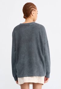 Oversized, donkergrijze trui van zachte, gestructureerde stof met verlaagde schouders en een brede halslijn. Heeft een relaxte pasvorm en een rechte zoom.